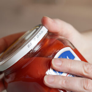 Glass jar of pickled tomatoes with white lid with expiration date. Woman Reads labels and looks at the expiration date Glass jar of pickled tomatoes with white lid with expiration date. Woman Reads labels and looks at the expiration date
