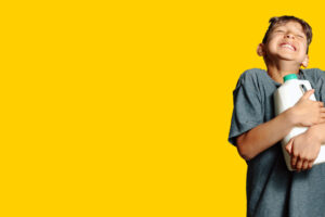 Boy hugging bottle of mild and smiling.