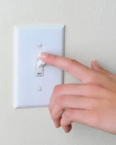 hand reaches to turn a white light switch mounted on a wall.