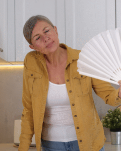woman uses a white hand fan to cool her face down